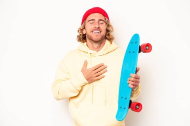 Beyaz arka plandaki beyaz tenli genç kaykaycı elini göğsünde tutarak kahkahalar atıyor..