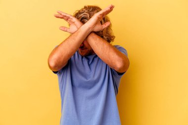 Sarı arka planda izole genç beyaz adam iki kolu çapraz tutuyor, inkar kavramı.