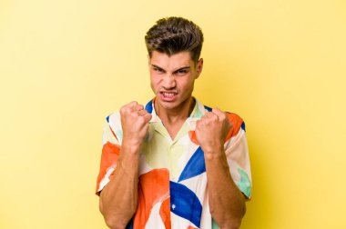 Sarı arka planda izole edilmiş genç beyaz adam kameraya yumruk gösteriyor, agresif yüz ifadesi var..