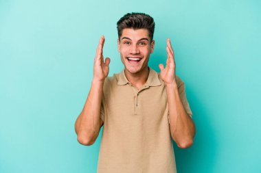 Mavi arka planda izole olmuş genç beyaz adam yüksek sesle gülüyor ve elini göğsüne koyuyor..