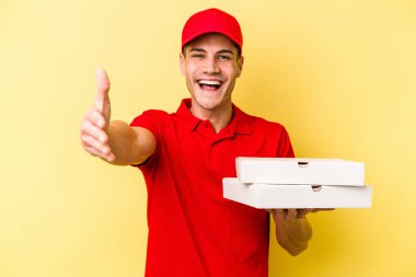 Young delivery caucasian man holding pizzas isolated on yellow background receiving a pleasant surprise, excited and raising hands.
