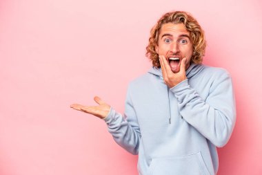 Pembe arka planda izole edilmiş genç beyaz bir adam avucunun içinde fotokopi alanı tutuyor, el üstünde tutuyor. Şaşırmış ve mutlu..