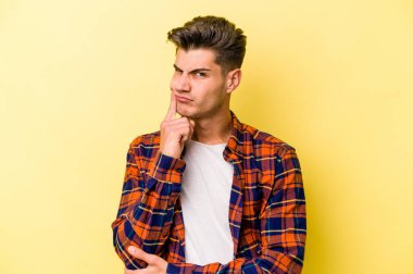 Sarı arka planda izole edilmiş genç beyaz adam alaycı bir ifadeyle kameraya bakıyor..