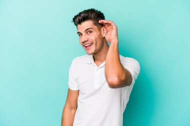 Mavi arka planda izole edilmiş genç beyaz adam bir dedikoduyu dinlemeye çalışıyor..