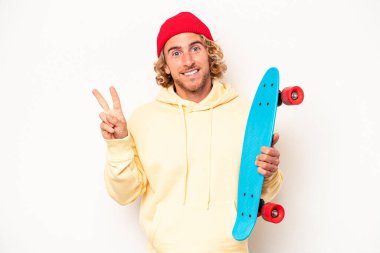 Beyaz arka planda izole edilmiş genç kaykaycı beyaz adam neşeli ve kaygısız parmaklarıyla barış sembolü gösteriyor..