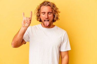 Sarı arka planda izole edilmiş genç beyaz adam parmaklarıyla kaya hareketi gösteriyor.