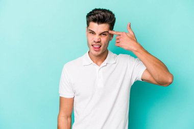 Mavi arka planda izole edilmiş genç beyaz adam işaret parmağıyla bir hayal kırıklığı jesti gösteriyor..