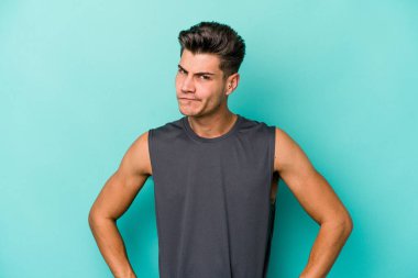 Kafkasyalı genç adam mavi arka planda izole, kafası karışmış, şüpheli ve güvensiz hissediyor..