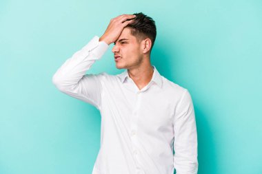 Kafkasyalı genç adam mavi arka planda izole edilmiş bir şekilde bir şeyi unutuyor. Alnına avuç içi ve gözlerini kapayarak vuruyor..