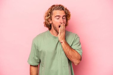 Pembe arka planda izole edilmiş genç beyaz adam esniyor. Ağzı eliyle kapatan yorgun bir hareket sergiliyor..