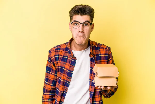 Mladý Běloch Drží Burger Izolovaný Žlutém Pozadí Pokrčí Rameny Otevřené — Stock fotografie
