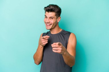 Mavi arka planda izole edilmiş genç beyaz adam parmaklarıyla ön tarafı işaret ediyor..