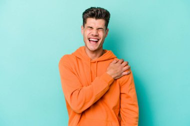 Mavi arka planda izole edilmiş, omuz ağrısı olan genç beyaz bir adam..