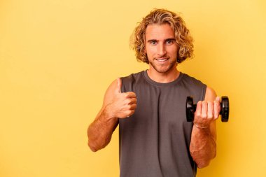 young sport man making weightlifting isolated on yellow background smiling and raising thumb up