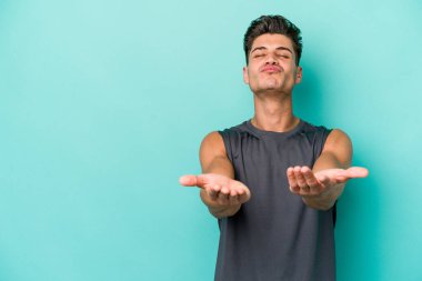 Kafkasyalı genç adam mavi arka planda izole edilmiş dudaklar kıvrılıyor ve hava öpücüğü göndermek için avuç içleri tutuyor..