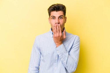 Sarı arka planda izole edilmiş genç beyaz adam şok olmuş, ağzı ellerle kaplanmış, yeni bir şey keşfetmeye hevesli..