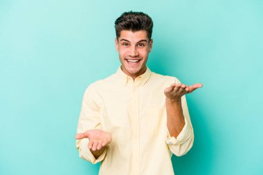 Mavi arka planda izole genç beyaz adam kollarıyla ölçek yapar, mutlu ve kendinden emin hisseder..