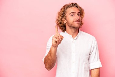 Pembe arka planda izole edilmiş genç beyaz bir adam bir numarayı parmağıyla gösteriyor..