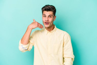 Mavi arka planda izole edilmiş genç beyaz bir adam bir şeye gülüyor, ağızlarını ellerle kapatıyor..