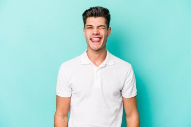 Kafkasyalı genç adam mavi arka planda izole edilmiş komik ve dost canlısı bir dil uzatıyor..