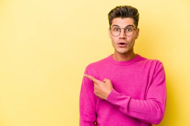 Sarı arka planda izole edilmiş genç beyaz adam yan tarafı işaret ediyor.