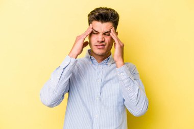 Sarı arka planda izole edilmiş genç beyaz adam tapınaklara dokunuyor ve baş ağrısı çekiyor..