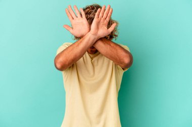 Kafkasyalı genç adam mavi arka planda izole edilmiş iki kolu çapraz tutuyor, inkar kavramı.