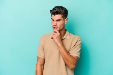 Kafkasyalı genç bir adam mavi arka planda izole edilmiş. Bir strateji planlıyor, bir iş yolu düşünüyor..