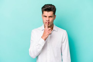 Mavi arka planda izole edilmiş genç beyaz bir adam ya sır saklıyor ya da sessizlik istiyor..