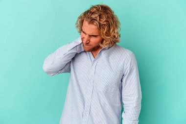 Kafkasyalı genç adam mavi arka planda izole edilmiş. Stres yüzünden boynu ağrıyor. Masaj yapıyor ve elle dokunuyor..
