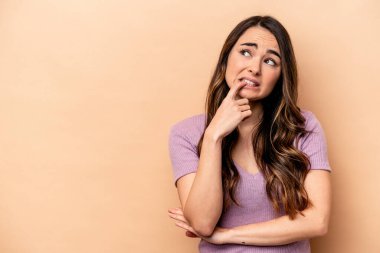 Beyazlı genç bir kadın bej arka planda izole edilmiş şüpheli ve şüpheci bir ifadeyle yana bakıyor..