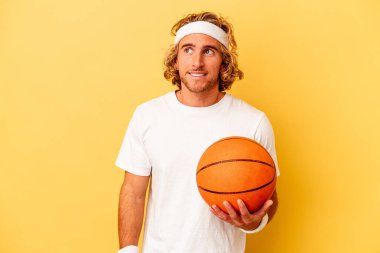 Genç basketbolcu beyaz adam sarı arka planda izole edilmiş hedeflere ve amaçlara ulaşma hayali kuruyor.