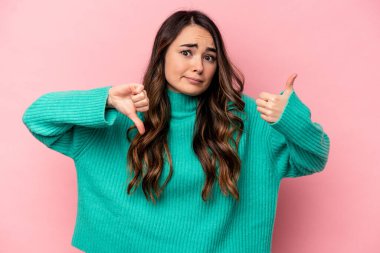 Pembe arka planda izole edilmiş genç beyaz kadın baş parmağını kaldırıyor ve baş parmağını aşağı gösteriyor, zor seçim kavramı.