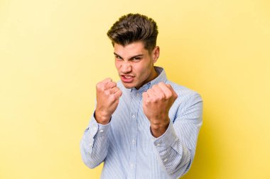 Sarı arka planda izole edilmiş genç beyaz bir adam bir tartışma yüzünden yumruk atıyor, öfkeleniyor, kavga ediyor, boks yapıyor.