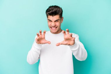 Mavi arka planda izole edilmiş genç beyaz adam pençelerini kedi taklidi yaparken gösteriyor, agresif bir hareket..