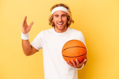 Genç basketbolcu beyaz adam sarı arka planda izole edilmiş. Hoş bir sürpriz, heyecanlı ve el kaldırıyor..