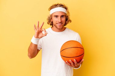Genç basketbolcu beyaz adam sarı arka planda izole edilmiş neşeli ve kendinden emin..