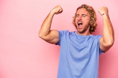 Pembe arka planda izole edilmiş genç beyaz adam zaferden sonra yumruğunu kaldırıyor, kazanan konsept..