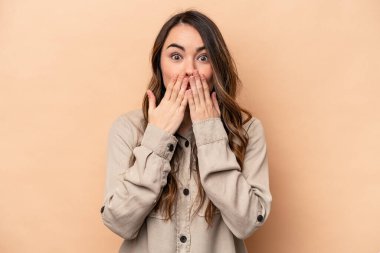 Beyazlı genç bir kadın bej arka planda izole edilmiş. Ağzını elleriyle kapatmış..
