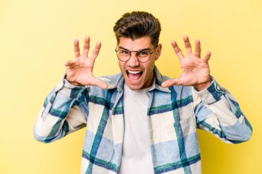 Sarı arka planda izole edilmiş genç beyaz adam pençelerini kedi taklidi yaparken gösteriyor, agresif bir hareket..