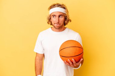 Young basketball player caucasian man isolated on yellow background confused, feels doubtful and unsure.