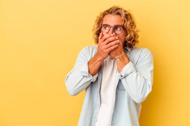 Kafkasyalı genç adam sarı arka planda izole edilmiş. Düşünceli bir şekilde, ağzını eliyle kapatan bir fotokopi odasına bakıyor..