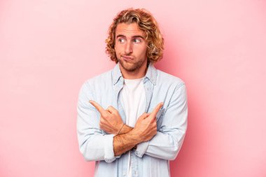 Pembe arka plan noktalarında izole edilmiş genç beyaz adam iki seçenek arasında seçim yapmaya çalışıyor..