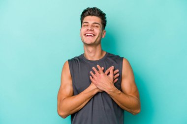 Mavi arka planda izole edilmiş beyaz bir genç, dost bir ifadeye sahip, avuçlarını göğsüne bastırıyor. Aşk konsepti.