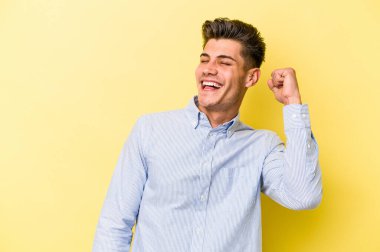 Sarı arka planda izole edilmiş genç beyaz adam zaferi, tutkuyu ve coşkuyu kutluyor, mutlu bir ifade..