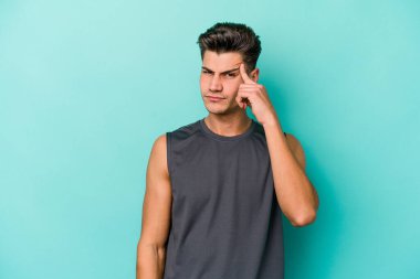 Mavi arka planda izole edilmiş genç beyaz bir adam şakağı parmağıyla işaret ediyor, düşünüyor ve bir göreve odaklanıyor..