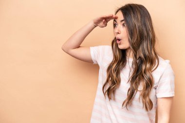 Beyazlı genç bir kadın bej arka planda izole edilmiş, uzaklara bakıyor ve elini alnına koyuyor..