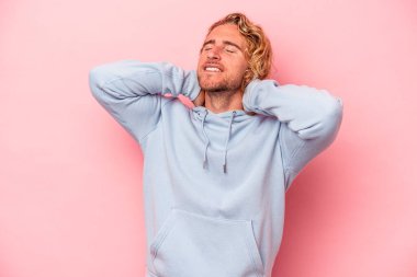 Pembe arka planda izole edilmiş genç beyaz bir adam kendini güvende hissediyor, elleri başının arkasında..