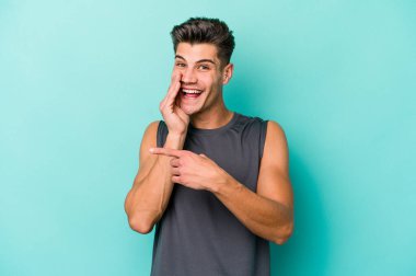 Kafkasyalı genç adam mavi arka planda izole edilmiş. Dedikodu yapıyor, bir şeyleri bildiriyor..