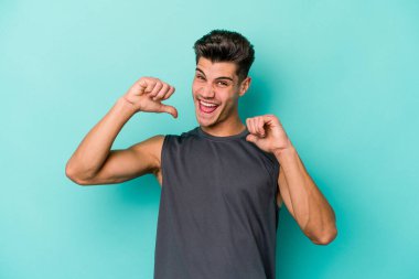 Mavi arka planda izole edilmiş genç beyaz adam gururlu ve kendinden emin hissediyor, örnek olarak.